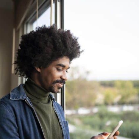 african american man at home by window using smart phone