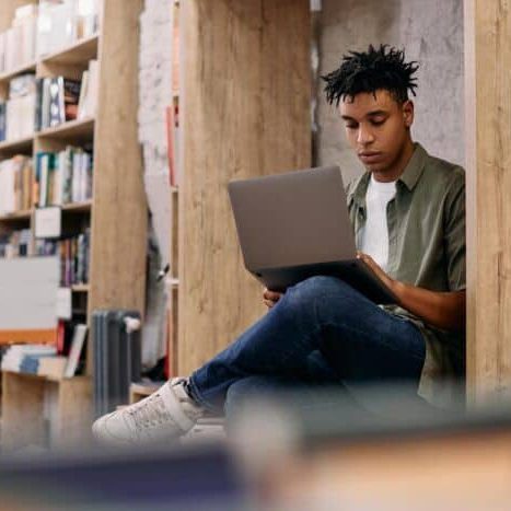 African American student e-learning on laptop during a research in a library.